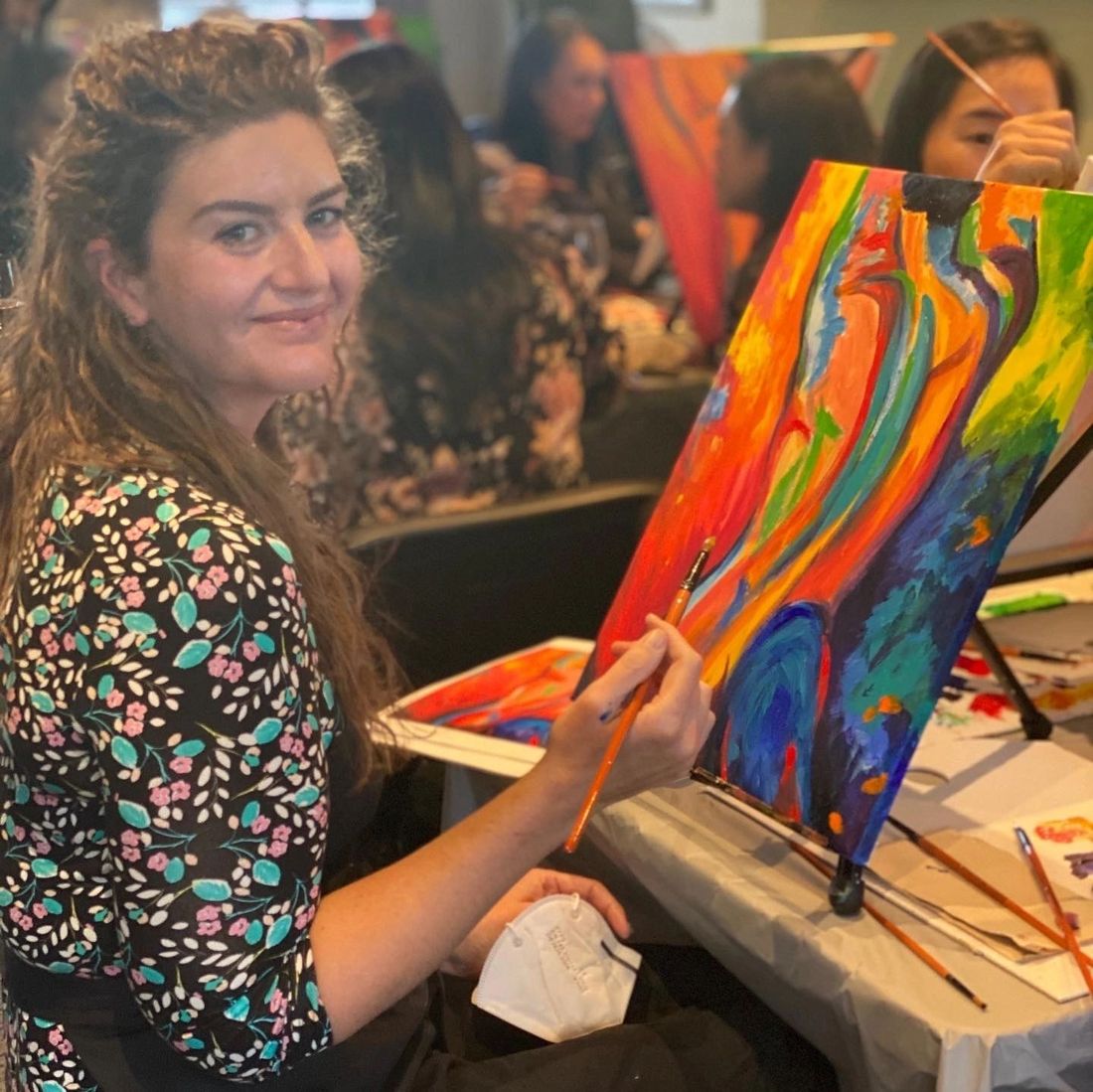 A guest smiling as she paints a colourful abstract