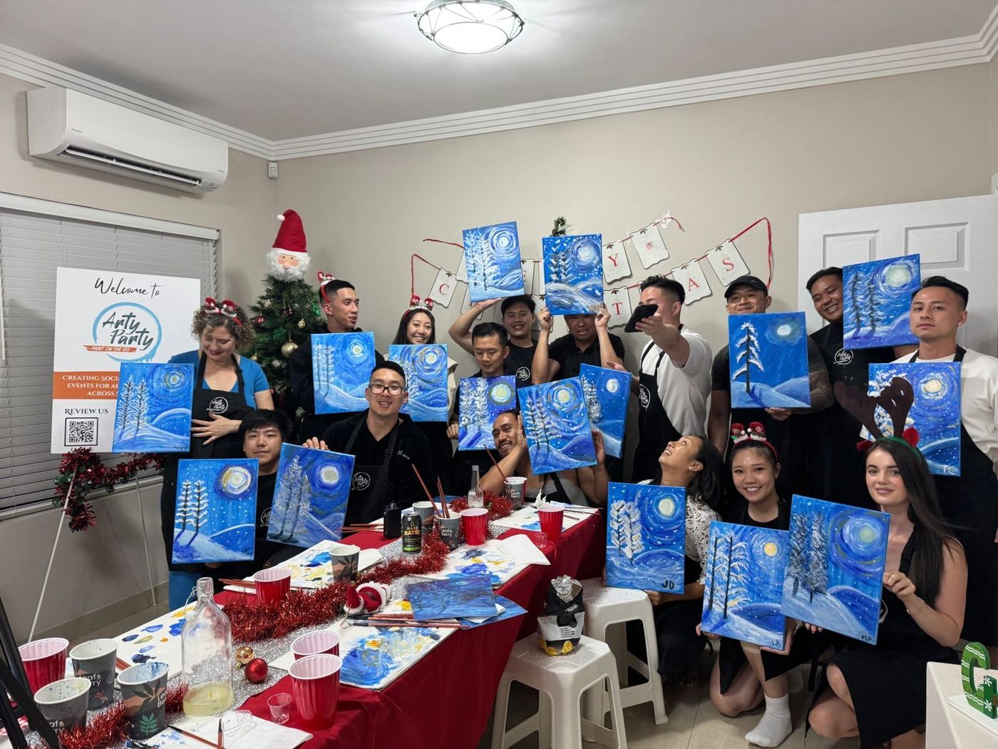 A team at a Christmas Arty Party holding their winter paintings